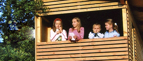 vier Kinder schauen aus einem Baumhaus von Geiger Holzbau
